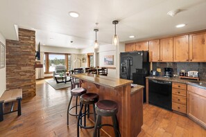 A spacious kitchen with wooden cabinets, a large island with stools, and a built-in dishwasher. - Serendipity | Includes Two 1-Day Lift Tickets (Tamarack)