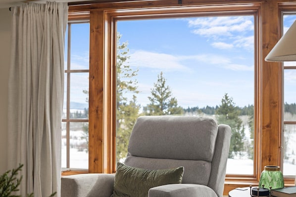 A room with a large window, a grey armchair, a green pillow, and a small table with a lamp. - Serendipity | Includes Two 1-Day Lift Tickets (Tamarack)