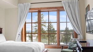 Ein Schlafzimmer mit großem Fenster, einem Bett, einem Sessel und einem Schreibtisch.