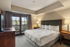 Hotelkamer met een groot bed, een bureau, een stoel, een nachtkastje, een lamp en uitzicht op het omliggende landschap door een raam.