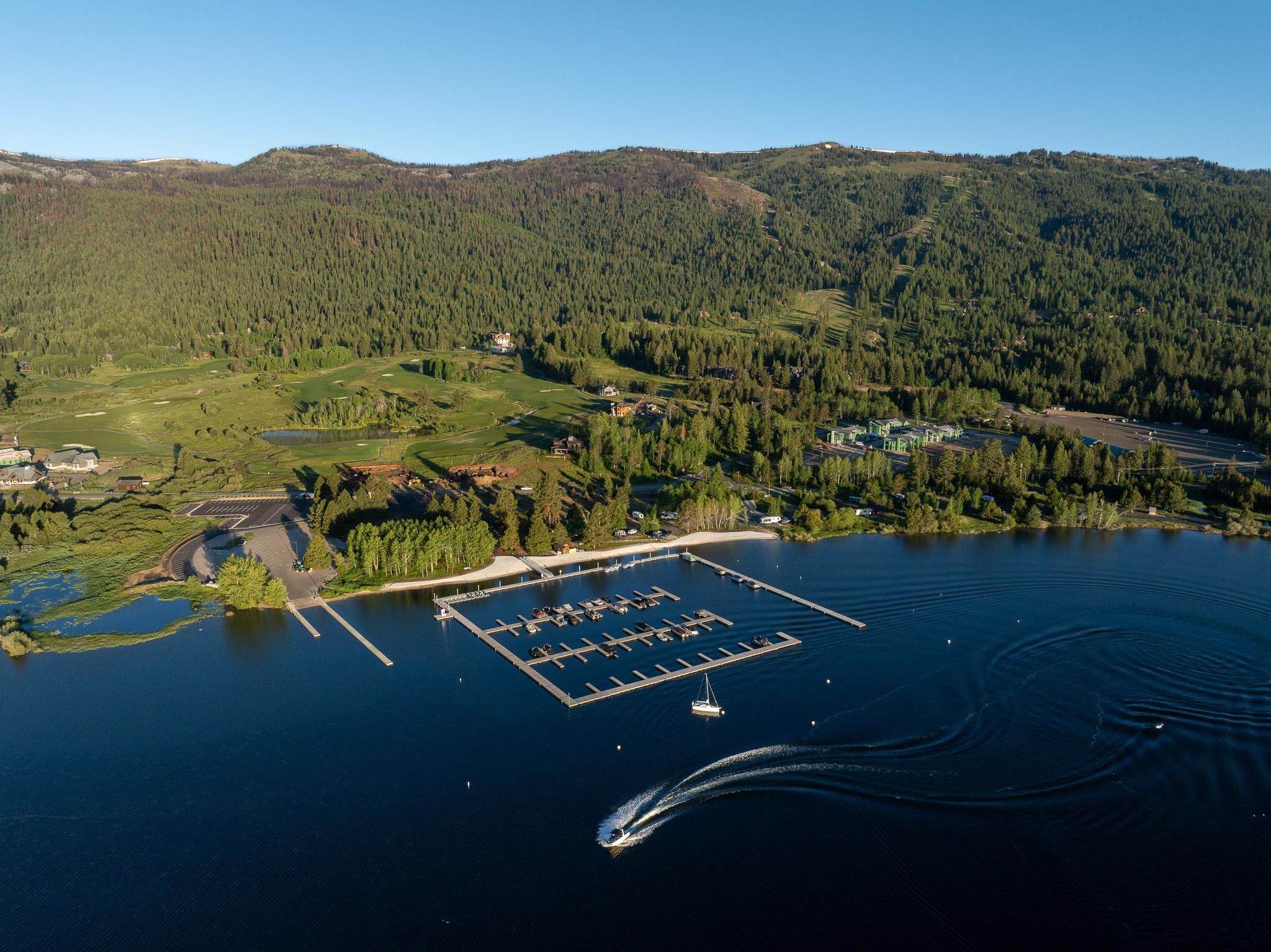 An aerial view of a lakeside property with a marina, golf course, and forested hills.