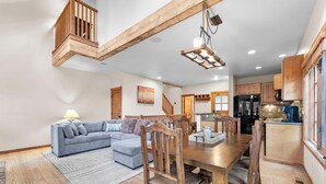 Ein geräumiges Wohnzimmer mit grauem Sofa, Esstisch aus Holz und Stühlen. Eine Treppe führt auf eine obere Ebene.
