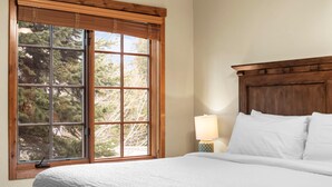 A bedroom with a large window, a wooden headboard, a bedside lamp, and a neatly made bed. - Base Camp | Includes Two 1-Day Lift Tickets (Tamarack)