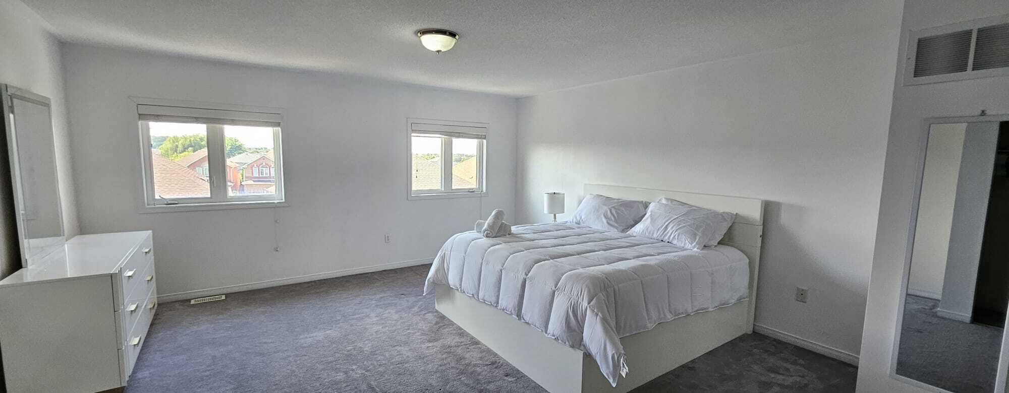 A bedroom with a bed, two windows, a dresser, and a ceiling light.