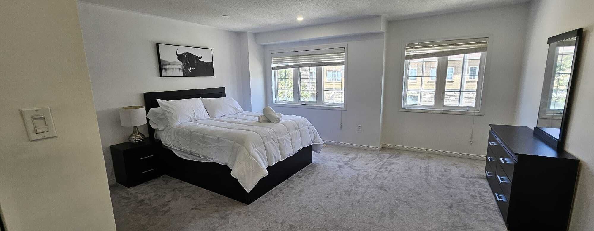 A bedroom with a bed, a nightstand, a dresser, and two windows.
