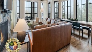 A spacious living area with a fireplace, large windows, and a high ceiling. - Calvi Penthouse | Includes Two 1-Day Lift Tickets (Tamarack)