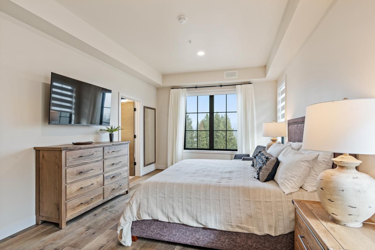A bedroom with a bed, a dresser, a TV mounted on the wall, and a window with curtains.