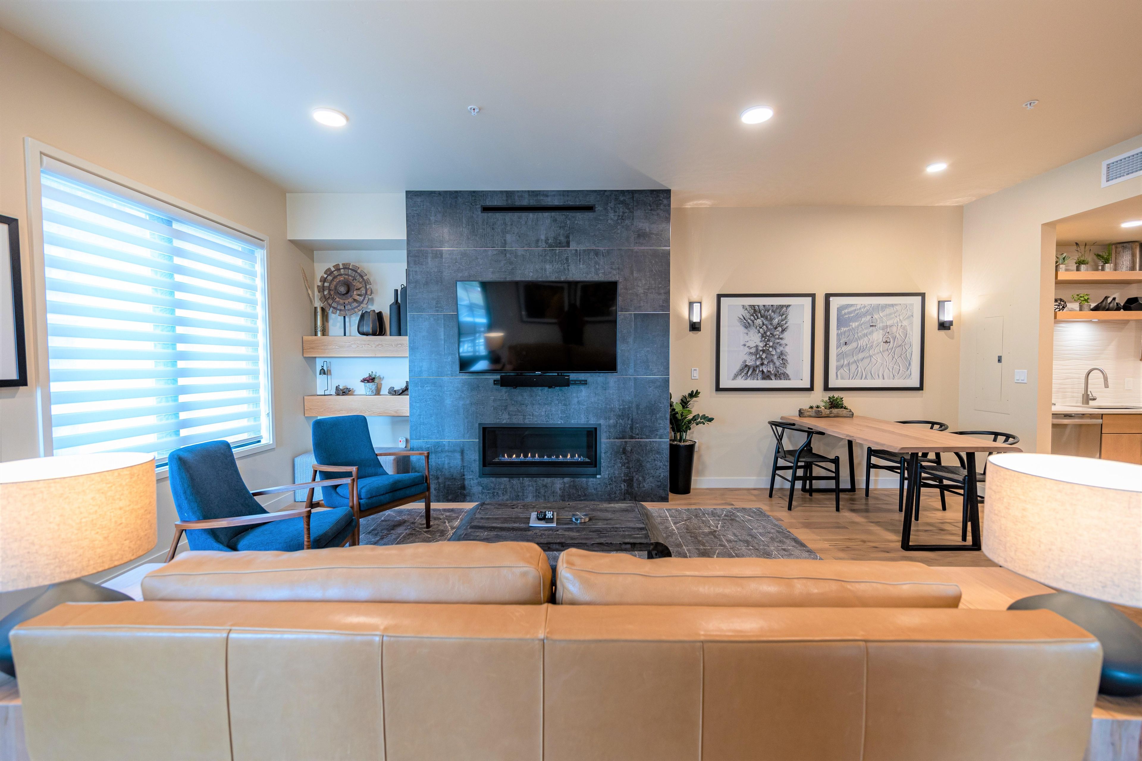 A modern living room with a fireplace, a TV mounted on the wall, and a dining area with a table and chairs.