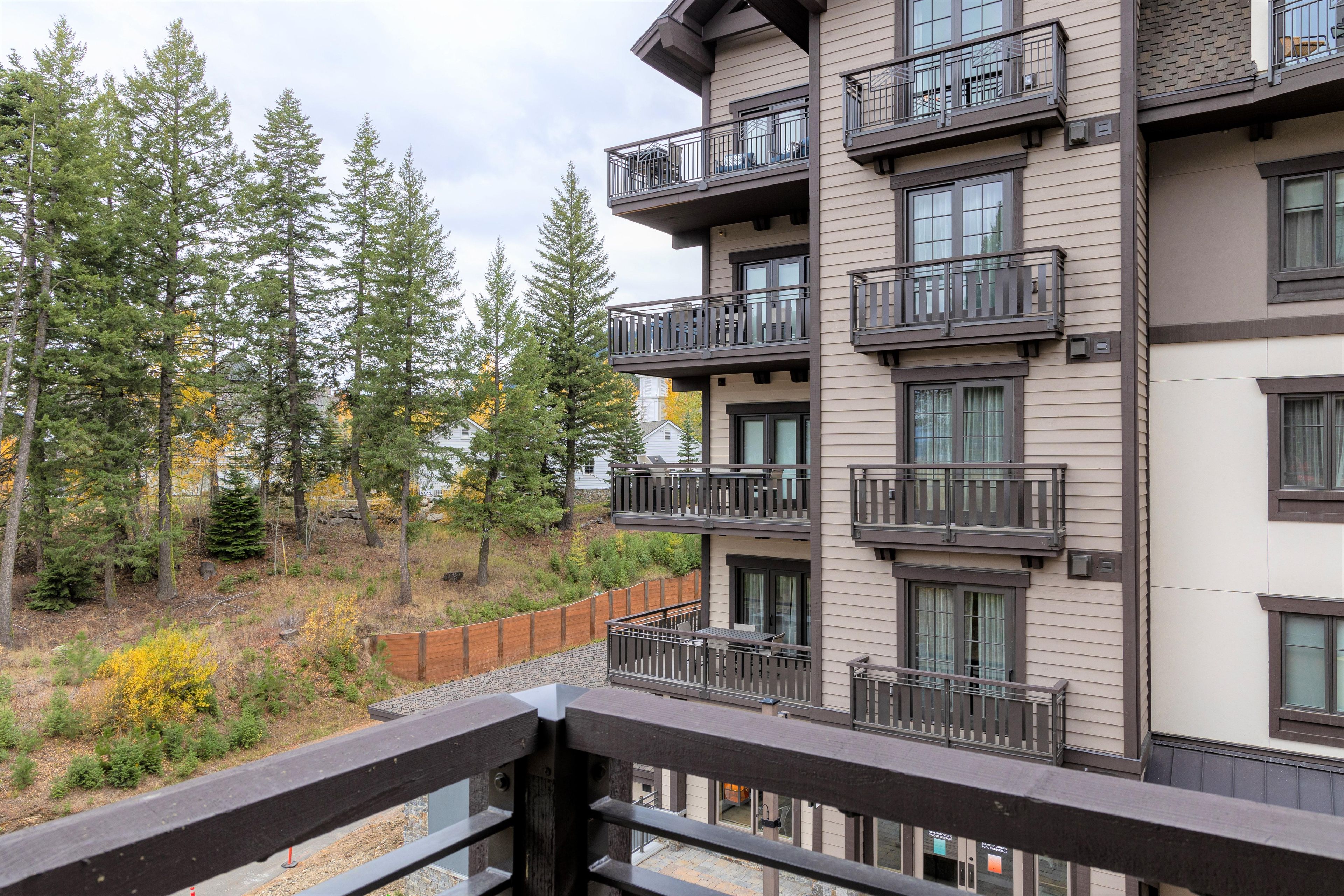 A multi-story building with balconies, surrounded by trees and a wooden fence.