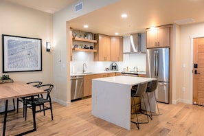 A modern kitchen with wooden cabinets, a stainless steel refrigerator, and a dining area with a table and chairs.