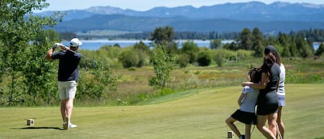 A golf course with a player preparing to hit a ball, a caddie, and a woman walking beside them.