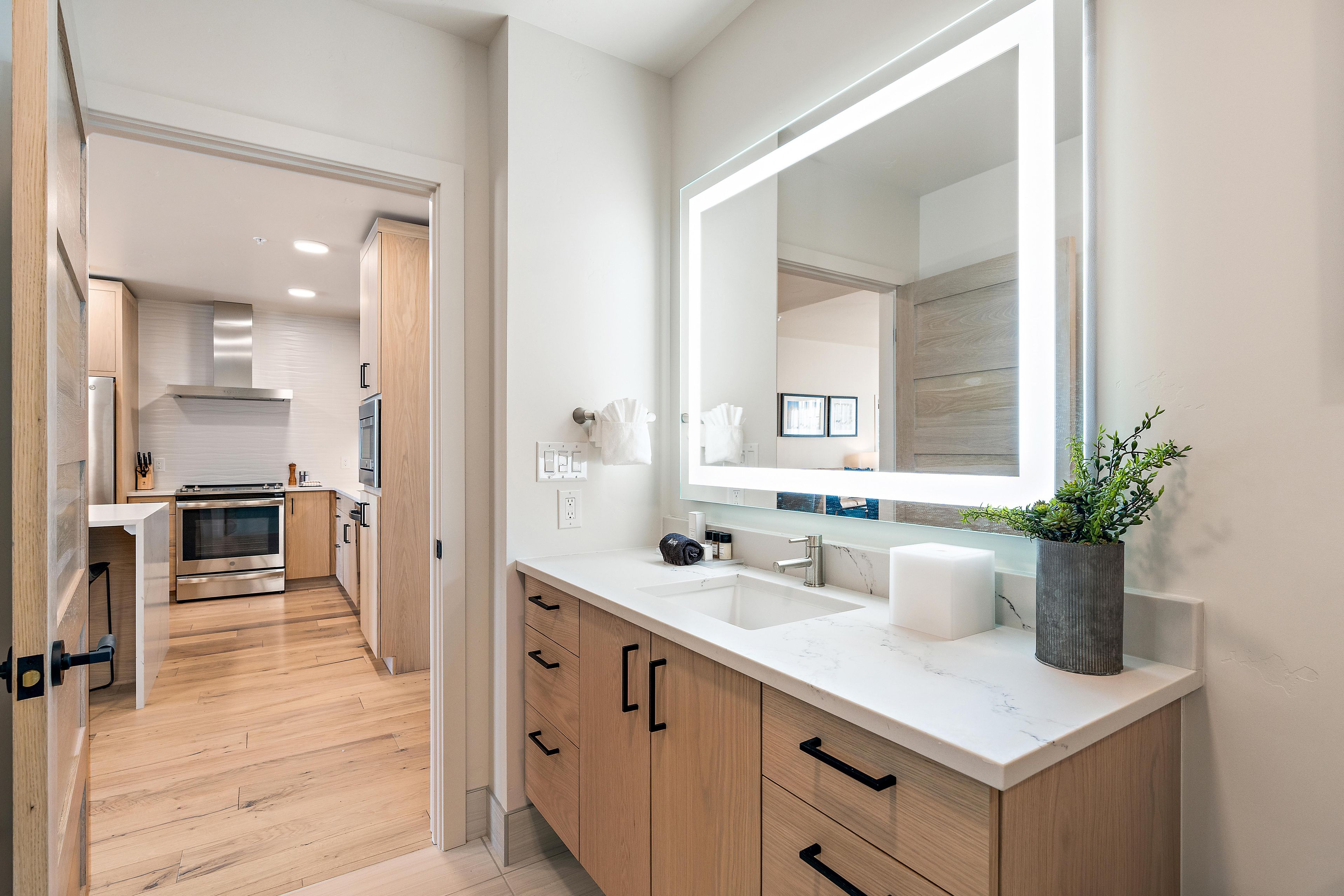 A modern bathroom with a large mirror, wooden cabinets, and a marble countertop.