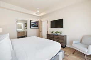 Un dormitorio con una cama grande, un aparador, una silla y un televisor de pantalla plana montado en la pared.