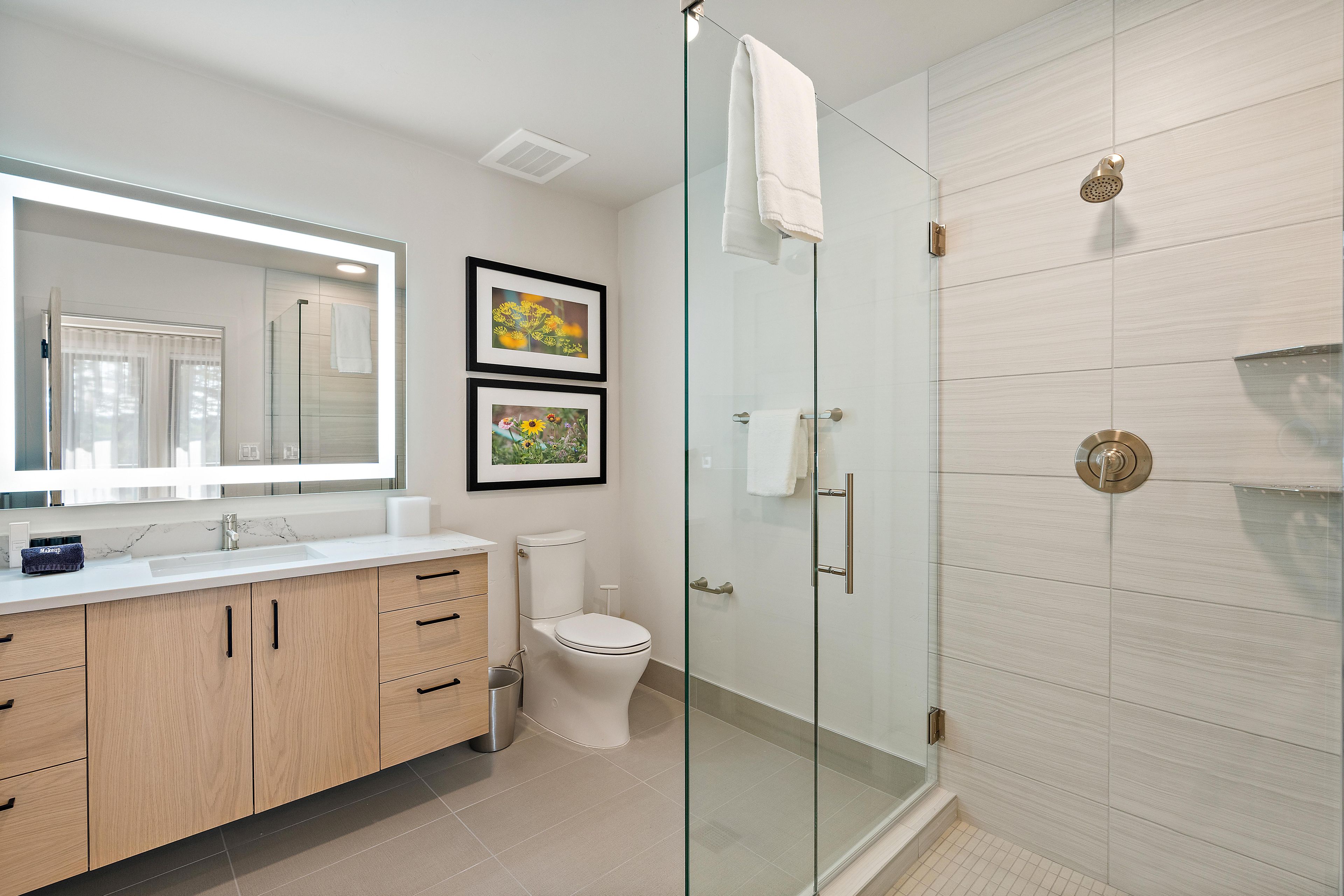 A modern bathroom with a glass shower enclosure, a toilet, and a vanity with a mirror and framed pictures.