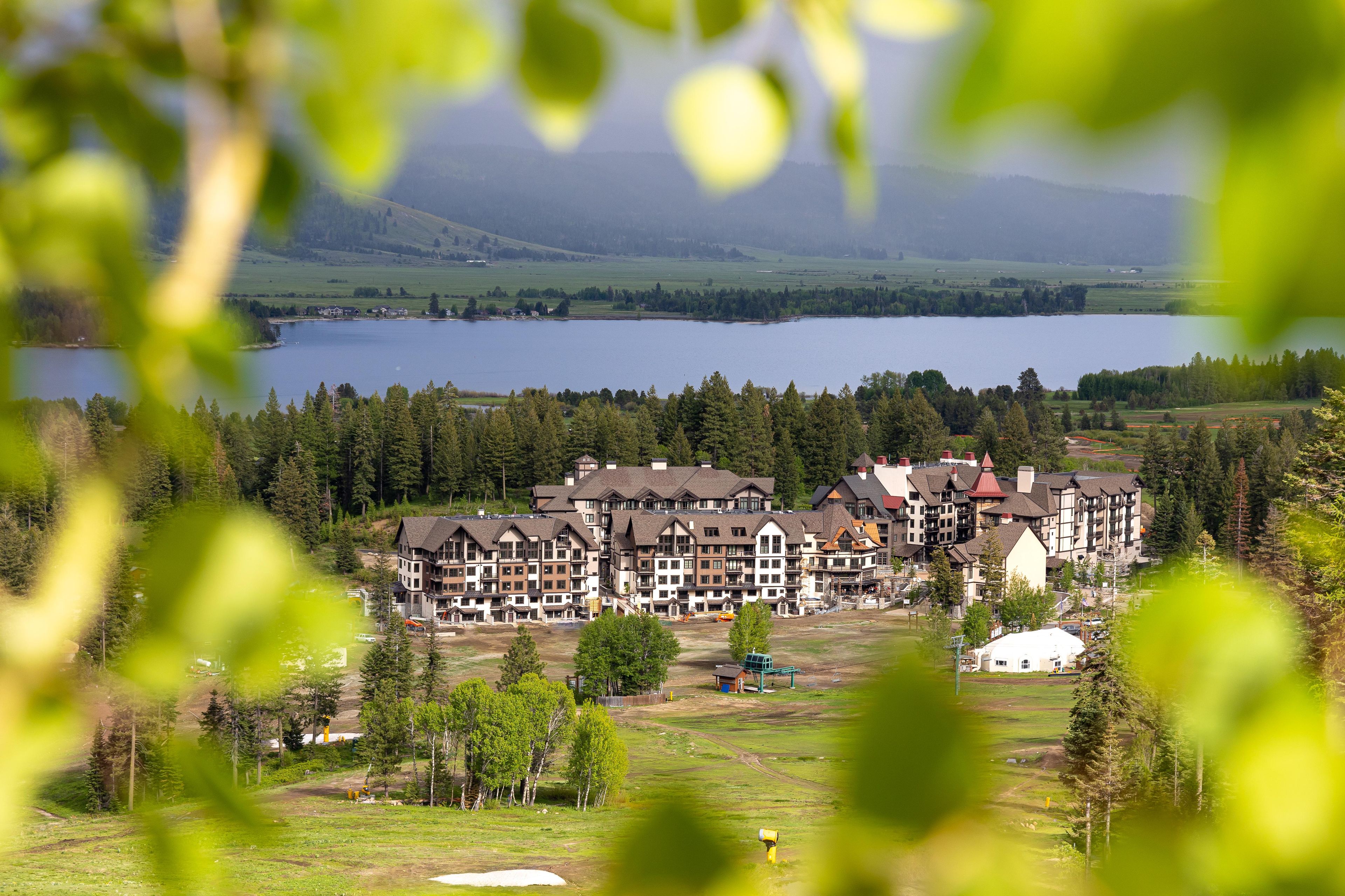 A multi-story hotel with a central courtyard, surrounded by a forested area and a lake.