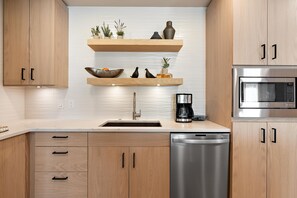 Una cocina moderna con armarios de madera, lavavajillas de acero inoxidable, microondas integrado y cafetera.