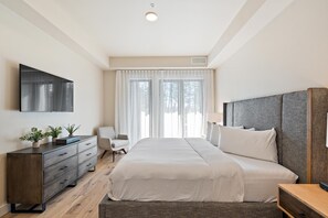 Un dormitorio moderno con cama, cómoda, una silla y televisor en la pared.