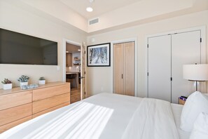 Un dormitorio con cama, cómoda, televisor y un cuadro en la pared.