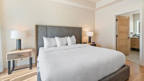 Una habitación de hotel con una cama grande, dos mesitas de noche, un armario y un baño visible a través de una puerta abierta.