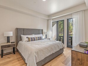 Quarto com cama grande, mesas de cabeceira e vista para o exterior através de uma porta de vidro deslizante.