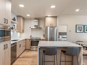 Eine moderne Küche mit Edelstahlgeräten, Holzschränken und einer zentralen Kochinsel mit Barhocker.