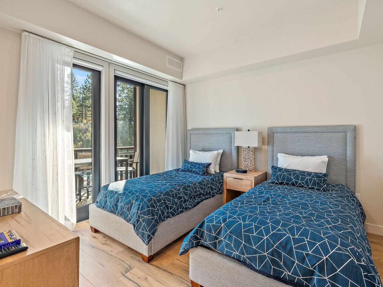 Une chambre d’hôtel avec deux lits, un bureau en bois, une table de chevet et une porte-fenêtre coulissante donnant sur un espace extérieur.