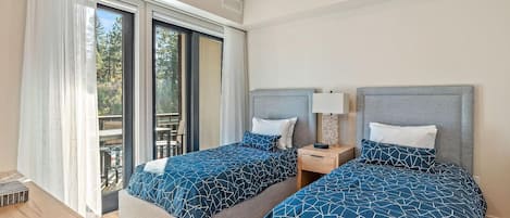 Habitación de hotel con dos camas, un escritorio de madera, una mesita de noche y un ventanal corredero que da a un espacio exterior.
