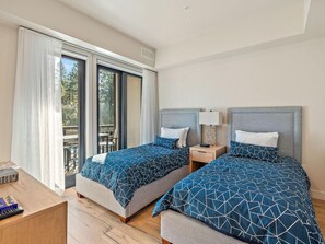 Une chambre d’hôtel avec deux lits, un bureau en bois, une table de chevet et une porte-fenêtre coulissante donnant sur un espace extérieur.