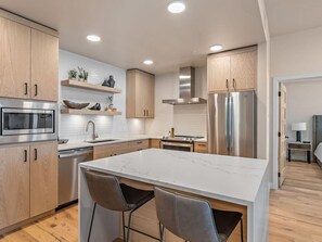 A modern kitchen with wooden cabinets, stainless steel appliances, and a marble countertop.