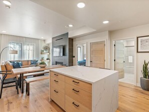 A modern kitchen with a marble countertop, wooden cabinets, and a dining area with a table and chairs.