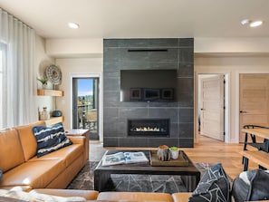 A modern living room with a fireplace, leather sofa, and a coffee table with magazines.