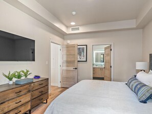 A bedroom with a bed, a dresser, a TV, and a bathroom visible through an open door. - Game Crossing | Includes Two 1-Day Lift Tickets (Tamarack)