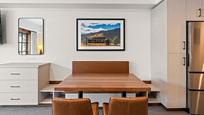 Una cocina moderna con una mesa de comedor de madera, dos sillas, un refrigerador y un cuadro de un paisaje en la pared.