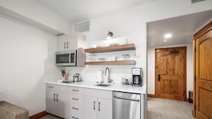 A compact kitchen with white cabinets, a stainless steel dishwasher, a microwave, and wooden shelves above the countertop. - Mossy Oak | Includes Two 1-Day Lift Tickets (Tamarack)