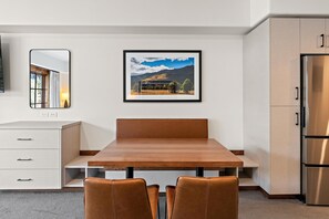 A modern kitchen with a wooden dining table, two chairs, a refrigerator, and a framed landscape picture on the wall. - Bear Den | Includes Two 1-Day Lift Tickets (Tamarack)