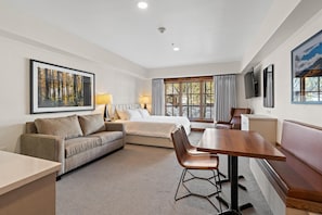 A hotel room with a bed, a sofa, a dining table, and a TV. - Bear Den | Includes Two 1-Day Lift Tickets (Tamarack)