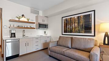 A modern kitchen with white cabinets, a microwave, and a coffee machine. There is a sofa and a framed picture on the wall.