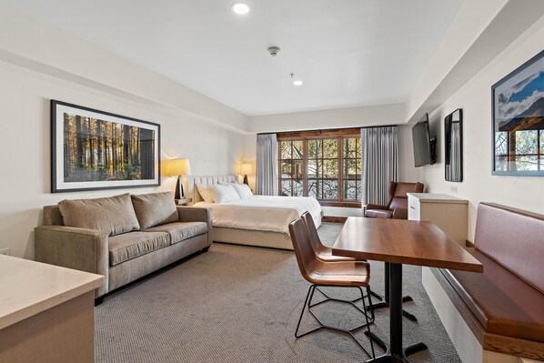 A hotel room with a bed, a sofa, a dining table, and a TV.