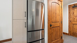 Un réfrigérateur en acier inoxydable dans une cuisine dotée d’armoires en bois et d’une porte en bois.