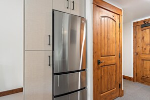 A stainless steel refrigerator in a kitchen with wooden cabinets and a wooden door.