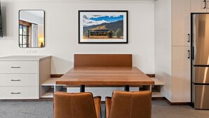 A modern kitchen with a wooden dining table, two chairs, a refrigerator, and a framed landscape picture on the wall. - Coyote Crossing | Includes Two 1-Day Lift Tickets (Tamarack)