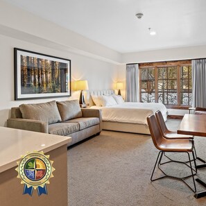 A hotel room with a bed, a sofa, a dining table, and a large window.