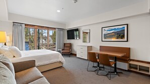 A hotel room with a bed, a desk, a chair, a TV, and a window with curtains. - Coyote Crossing | Includes Two 1-Day Lift Tickets (Tamarack)
