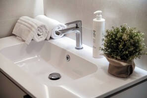 A white bathroom sink with a modern faucet, a rolled white towel, a bottle of lotion, and a small potted plant. - Luci A Lago (Como)