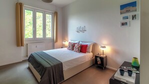 A bedroom with a bed, bedside lamps, a window with curtains, a radiator, and wall art. - Luci A Lago (Como)