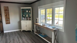 A room with a wooden floor, a white cabinet with glass doors, a window with a view of the outside, and a wall with a motivational quote.