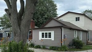 A single-story house with a grey siding exterior, a chimney, and a small porch.