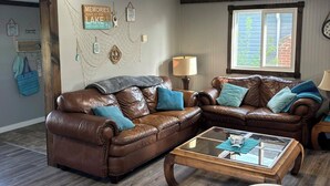 A living room with a brown leather sectional sofa, a glass coffee table, and a dining table with chairs.