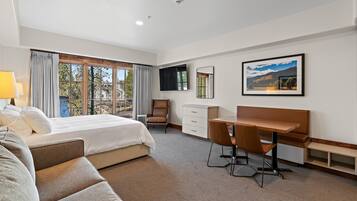 A hotel room with a bed, a desk, a chair, a TV, and a window with curtains.