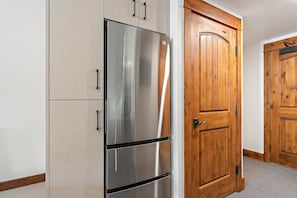 A stainless steel refrigerator in a kitchen with wooden cabinets and a wooden door. - Azure Lodge | Includes Two 1-Day Lift Tickets (Tamarack)